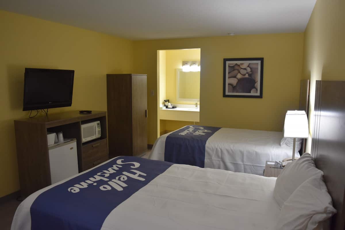 A hotel room with two beds, a television, a microwave, a refrigerator, a sink, and a mirror.