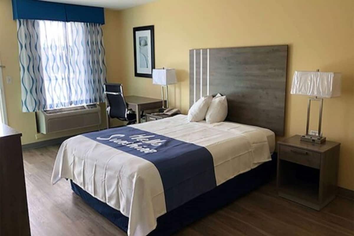 A hotel room with a bed, bedside tables, a desk, a chair, and a window with curtains.
