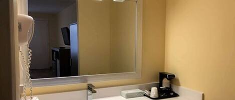 A hotel bathroom with a large mirror, a sink, a hairdryer, and a coffee machine.