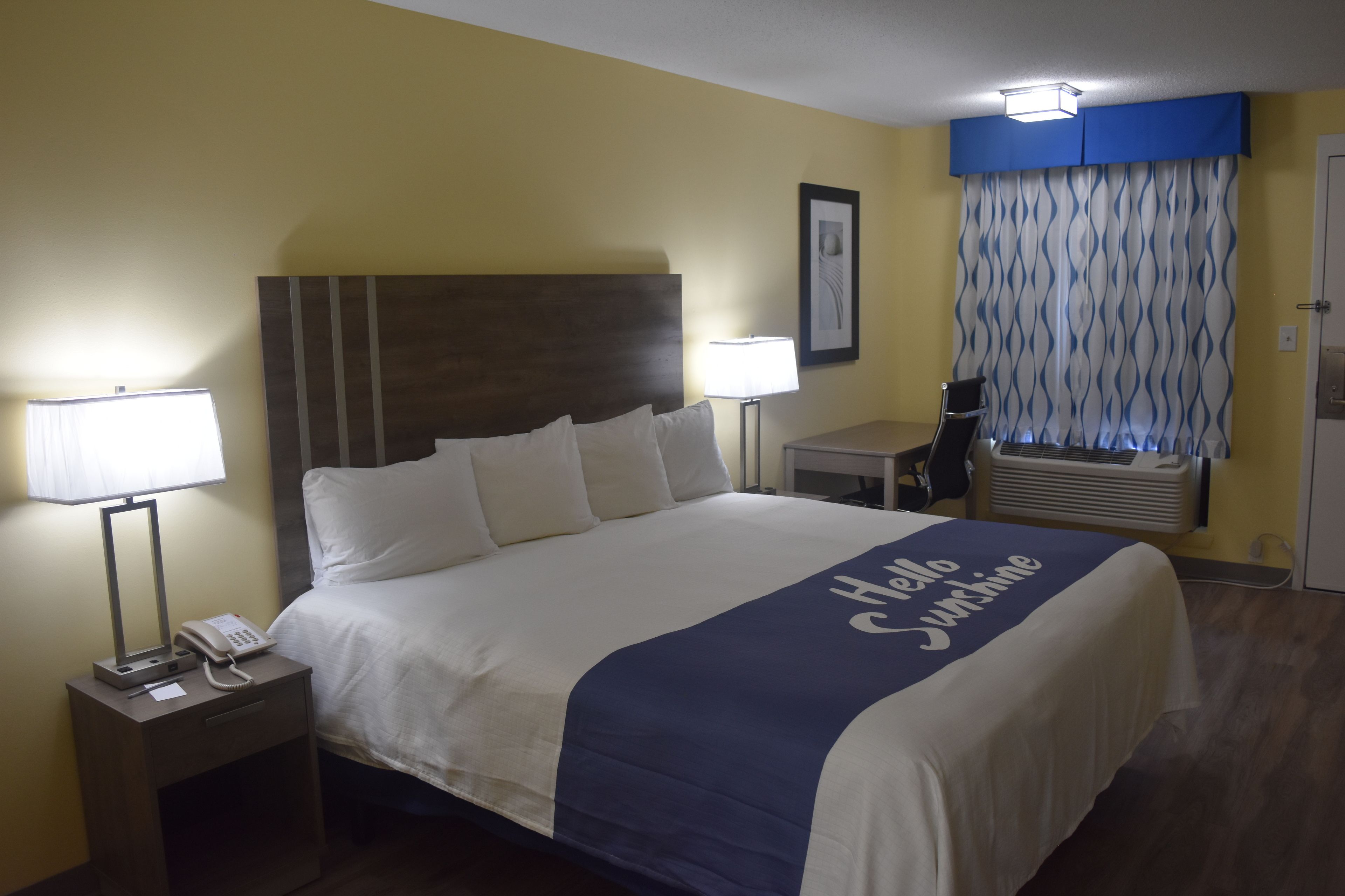 A hotel room with a bed, bedside lamps, a telephone, a desk, and a window with curtains.