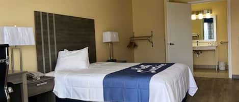 Hotelkamer met een bed, nachtkastjes, een bureau, een lamp, een spiegel en een zichtbare badkamer door een open deur.