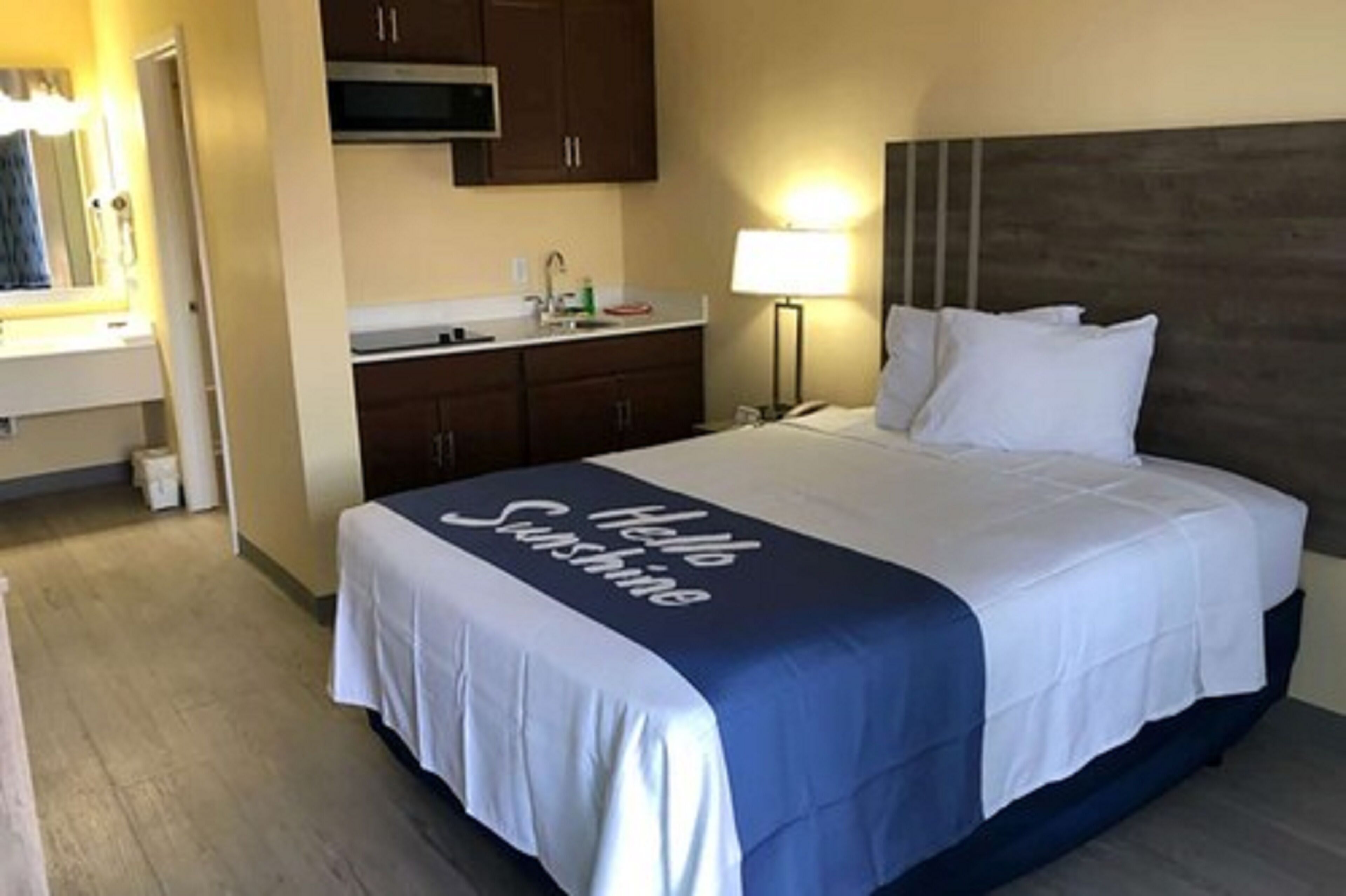 A hotel room with a bed, a nightstand, a lamp, a microwave, and a sink.