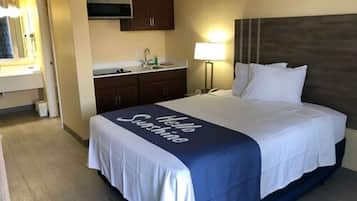 A hotel room with a bed, a nightstand, a lamp, a microwave, and a sink.