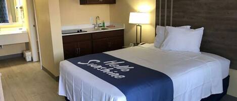 A hotel room with a bed, a nightstand, a lamp, a microwave, and a sink.