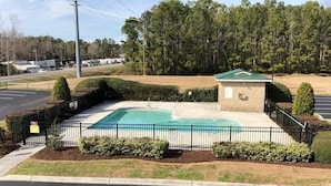 A swimming pool with a small building, surrounded by a fence and greenery.
