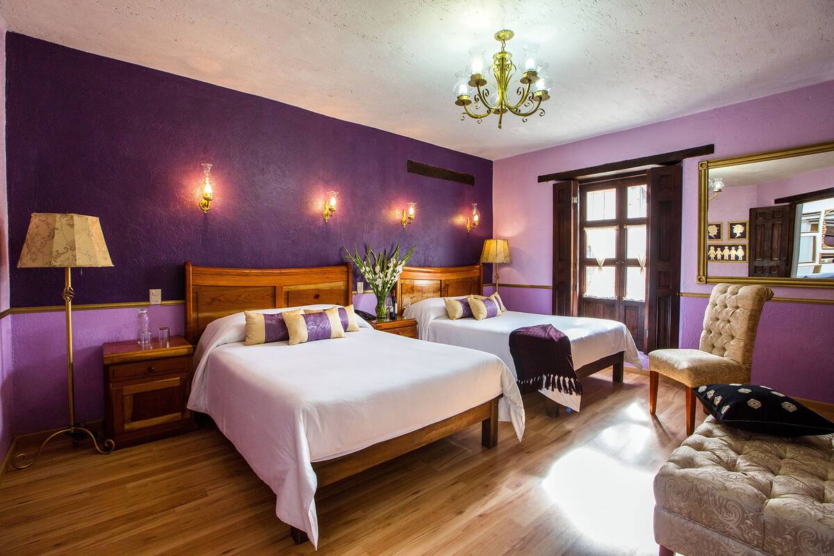 Una habitación con dos camas, una silla, una araña y apliques de pared.