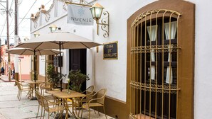 An outdoor seating area with tables and chairs, a sign for InnMense Hotels, and a window with decorative iron bars. - Grand Guadalupe by Inmense (San Cristóbal de las Casas)