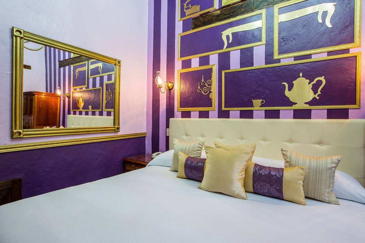 Una habitación de hotel con una cama grande, un espejo y una pared con cuadros.