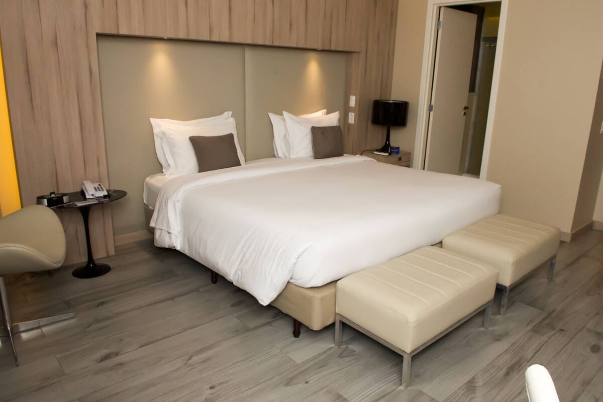 A modern hotel room with a large bed, bedside tables, a chair, and a bench.