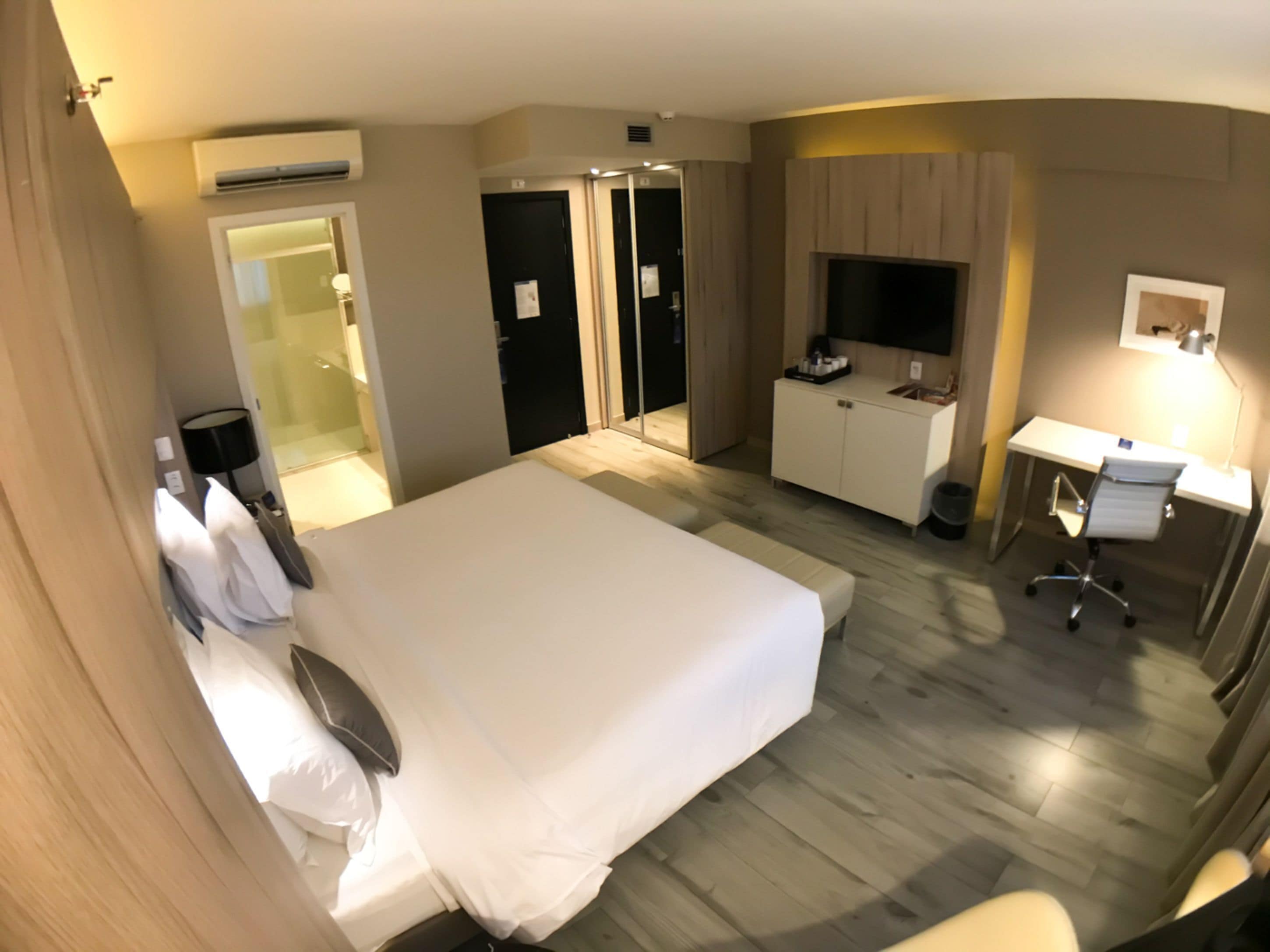 A hotel room with a large bed, a desk with a chair, a TV, and a wardrobe.