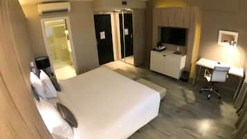 A hotel room with a large bed, a desk with a chair, a TV, and a wardrobe.