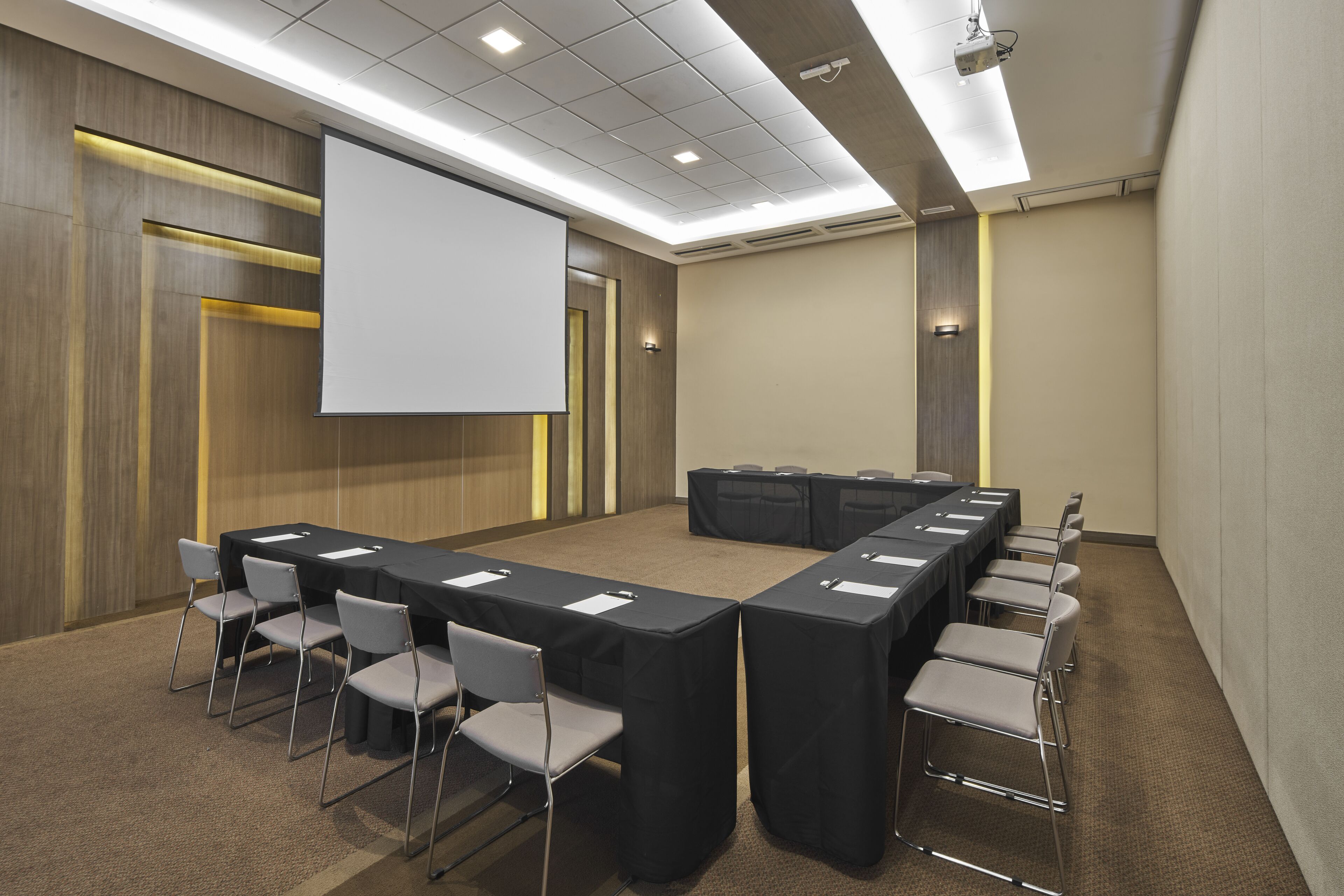 Una sala de conferències amb una taula llarga, cadires, una pantalla de projector i un sòl amb moqueta.