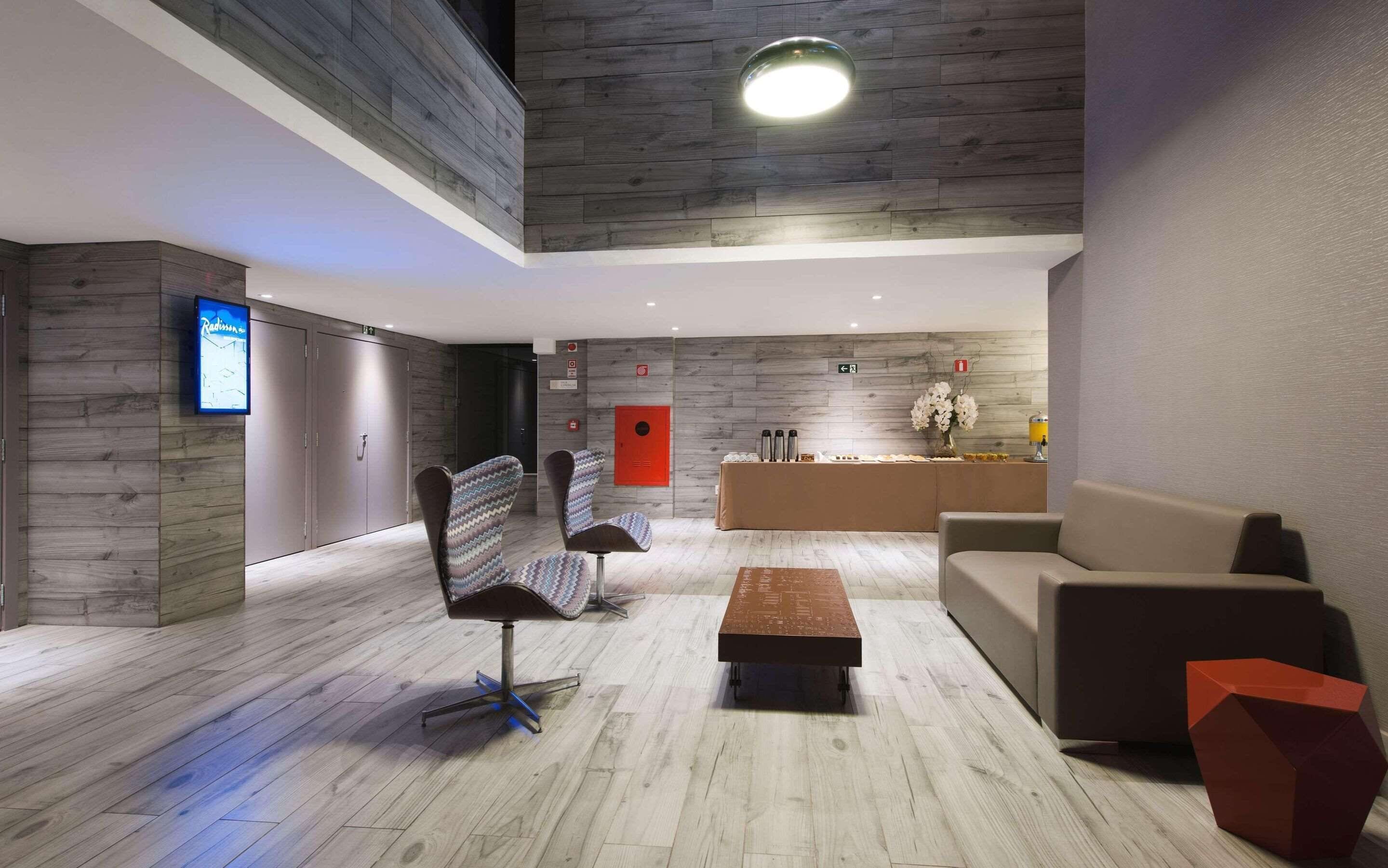 A modern lobby with a wooden floor, a reception desk, a sofa, and two chairs.