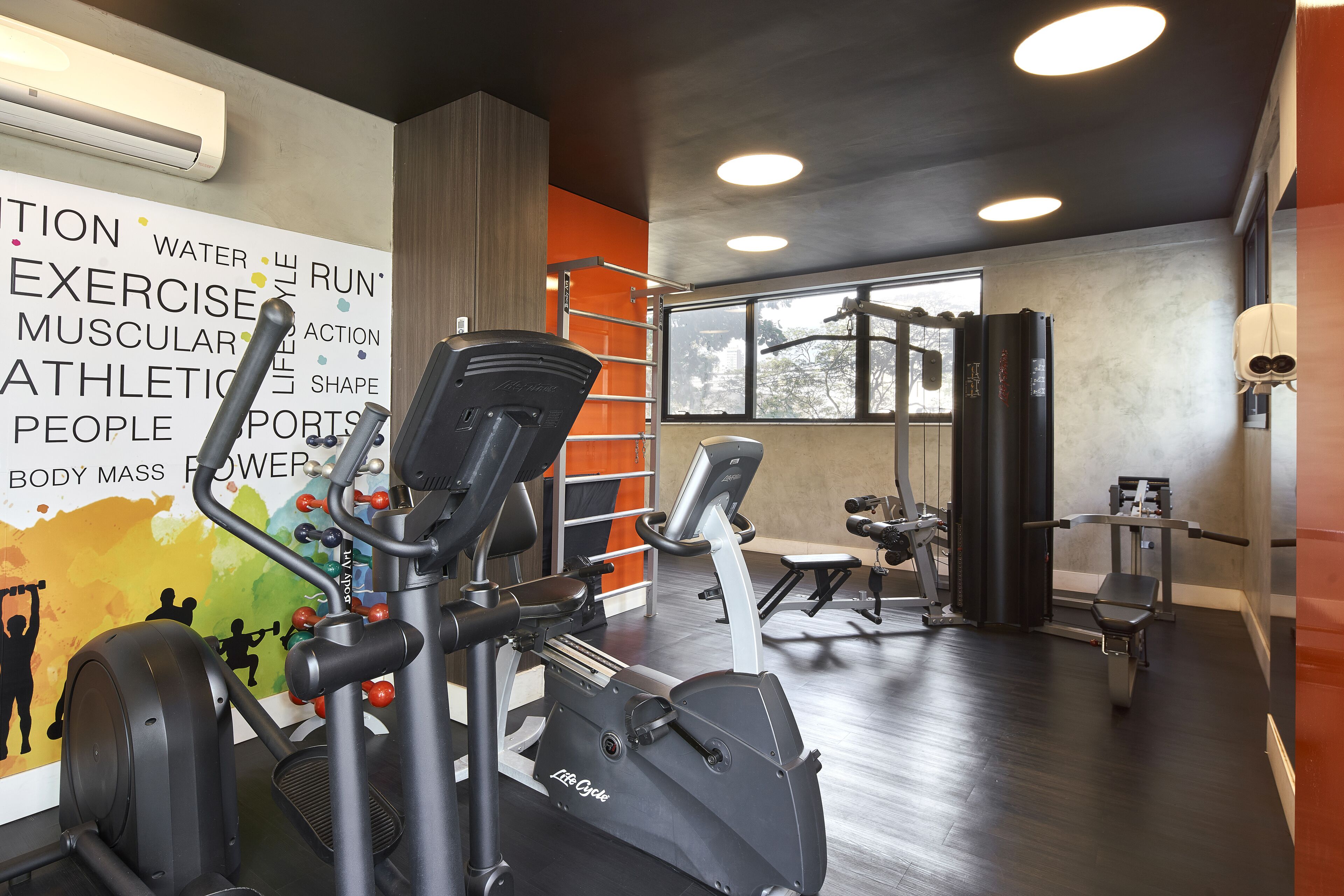 Een sportschool met trainingsapparatuur, een groot motiverend poster en een raam dat natuurlijk licht binnenlaat.