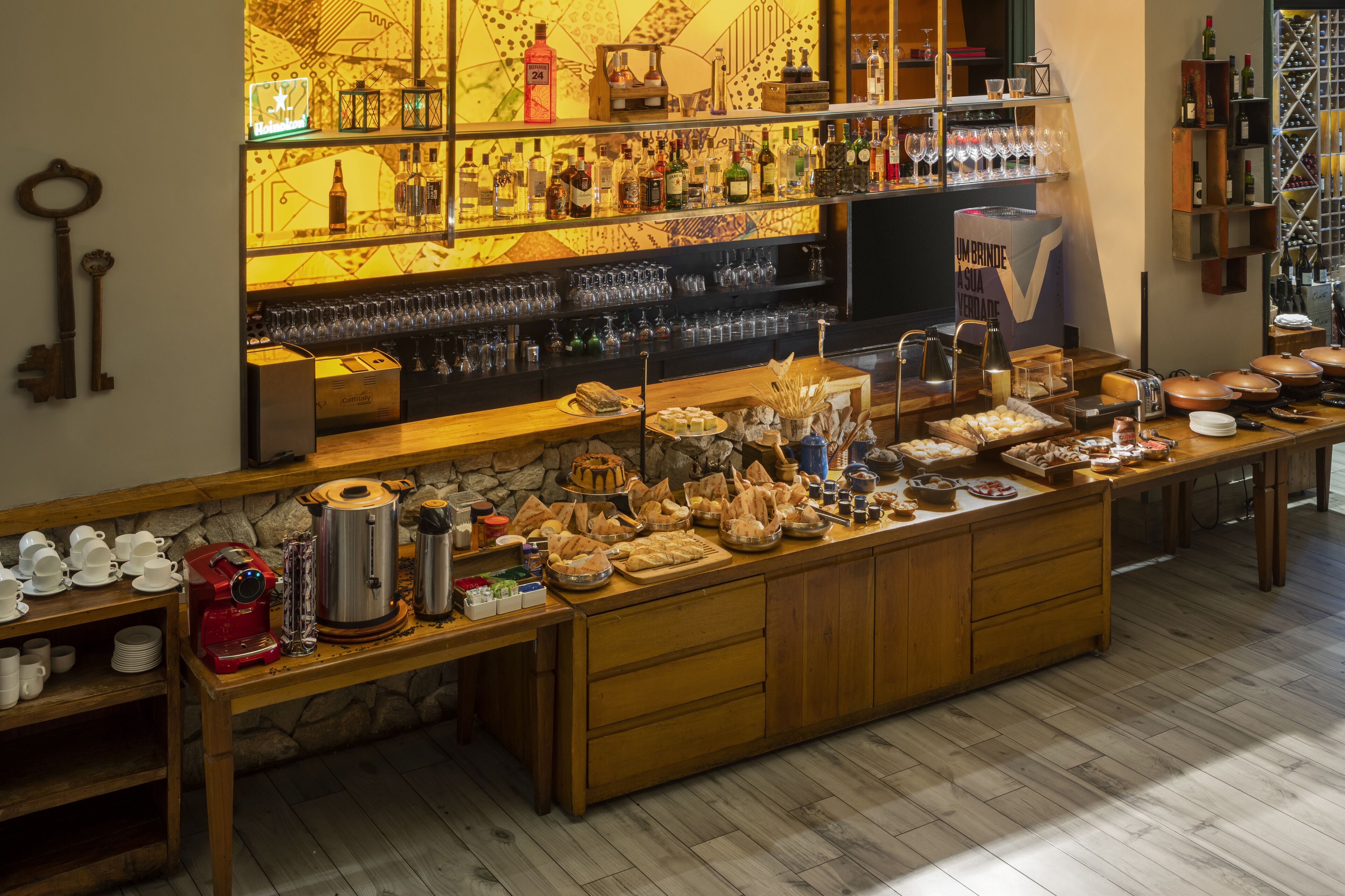 Zona de bar con estantes llenos de botellas, vasos y una máquina de café.