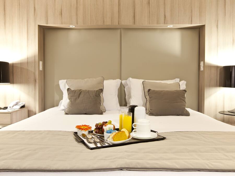 A neatly made bed with a tray of breakfast items, including toast, fruit, and juice, in a modern hotel room.