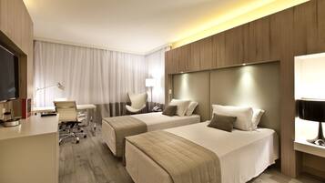 A hotel room with two beds, a desk, a chair, a TV, and a lamp.