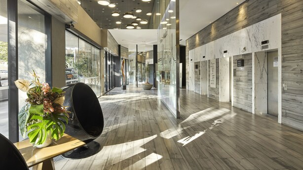 Un vestíbulo de hotel moderno con suelo de madera, una planta grande en maceta y una zona de estar.