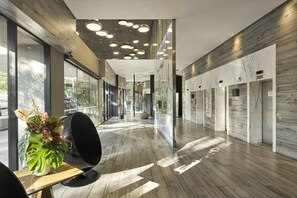 Un vestíbulo de hotel moderno con suelo de madera, una planta grande en maceta y una zona de estar.