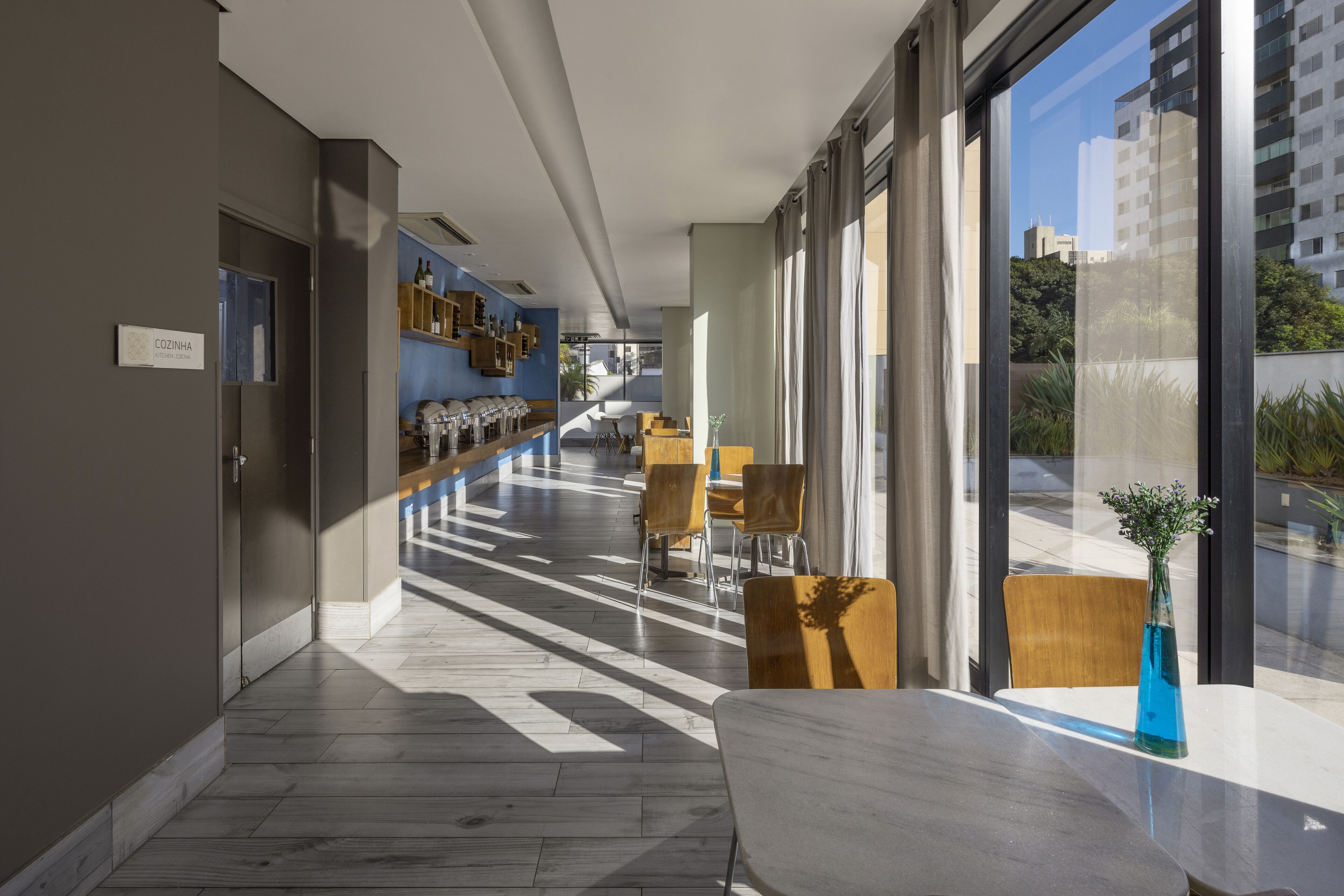 Un pasillo moderno de hotel con una zona de bar, asientos y grandes ventanales con vistas a la ciudad.