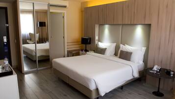 A hotel room with a large bed, a mirror, a bedside table with a lamp, and a small table with a phone and remote control.