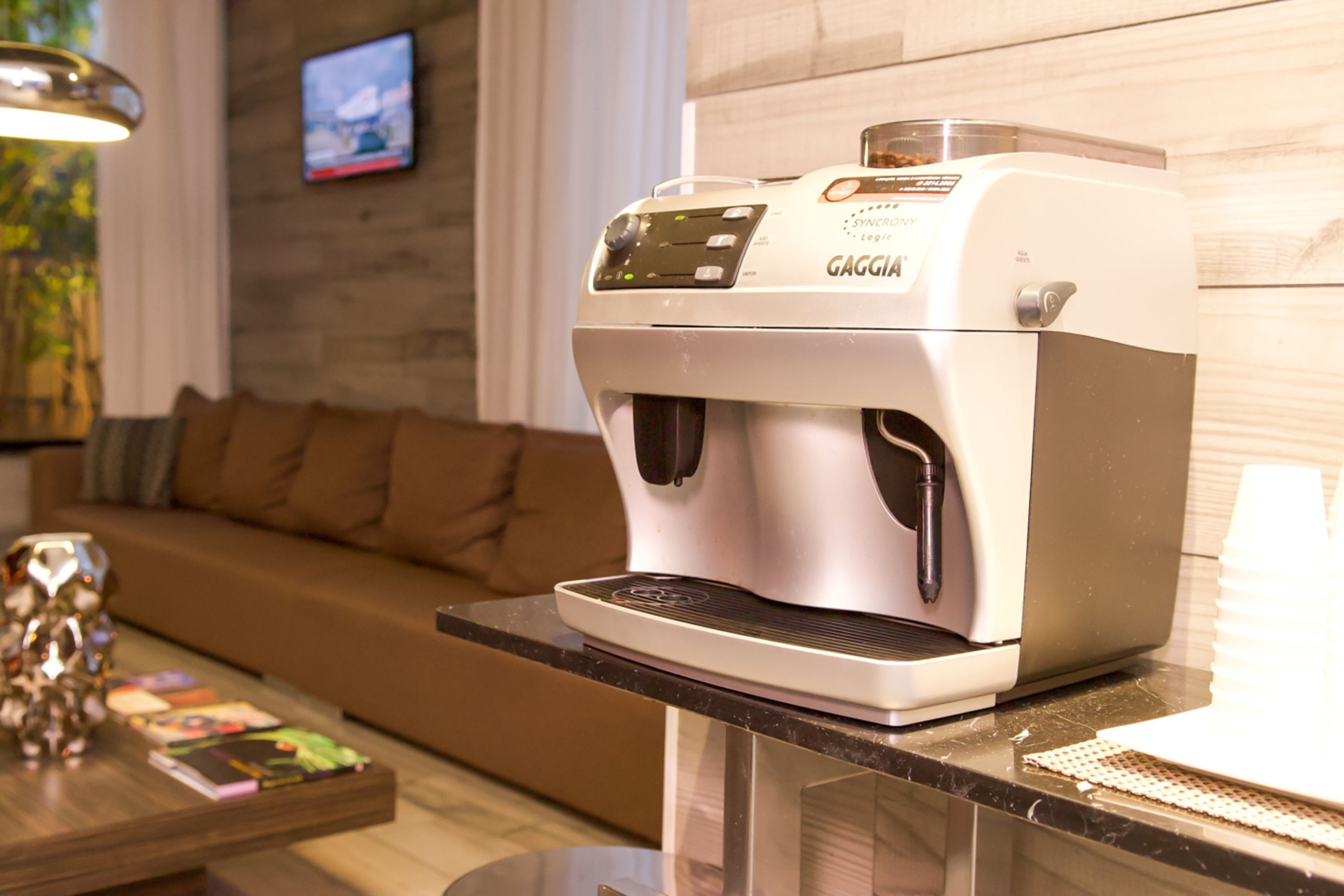 A coffee machine on a kitchen counter with a wooden wall and a brown sofa in the background.