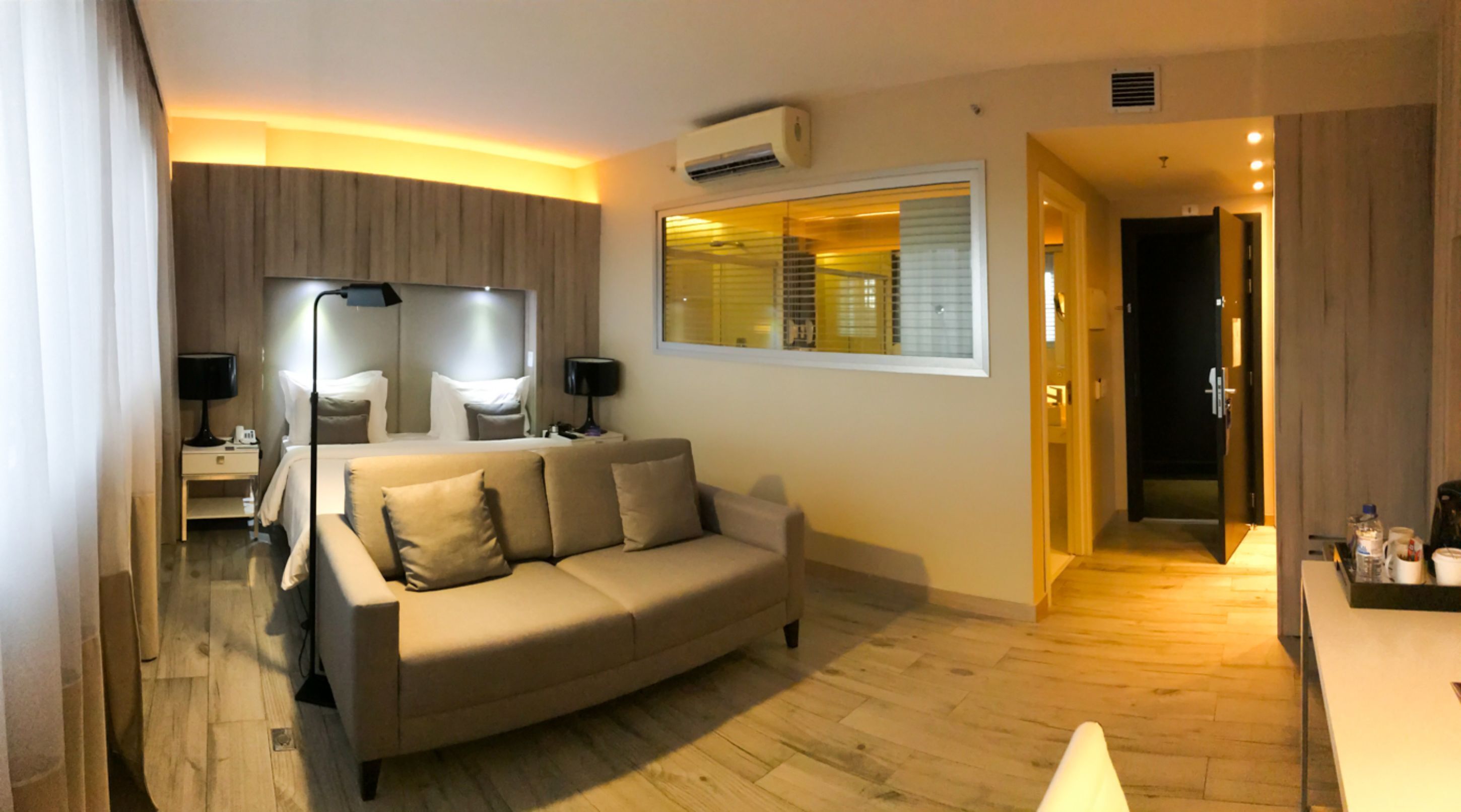 Una sala de estar moderna con un sofá color beige, un televisor de pantalla plana y un ventanal con persianas.