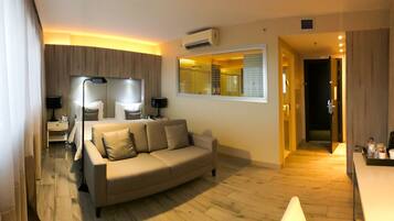 Una sala de estar moderna con un sofá color beige, un televisor de pantalla plana y un ventanal con persianas.