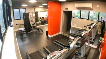 Une salle de sport équipée de tapis de course, d’appareils de musculation et d’un mur entièrement recouvert de miroirs.