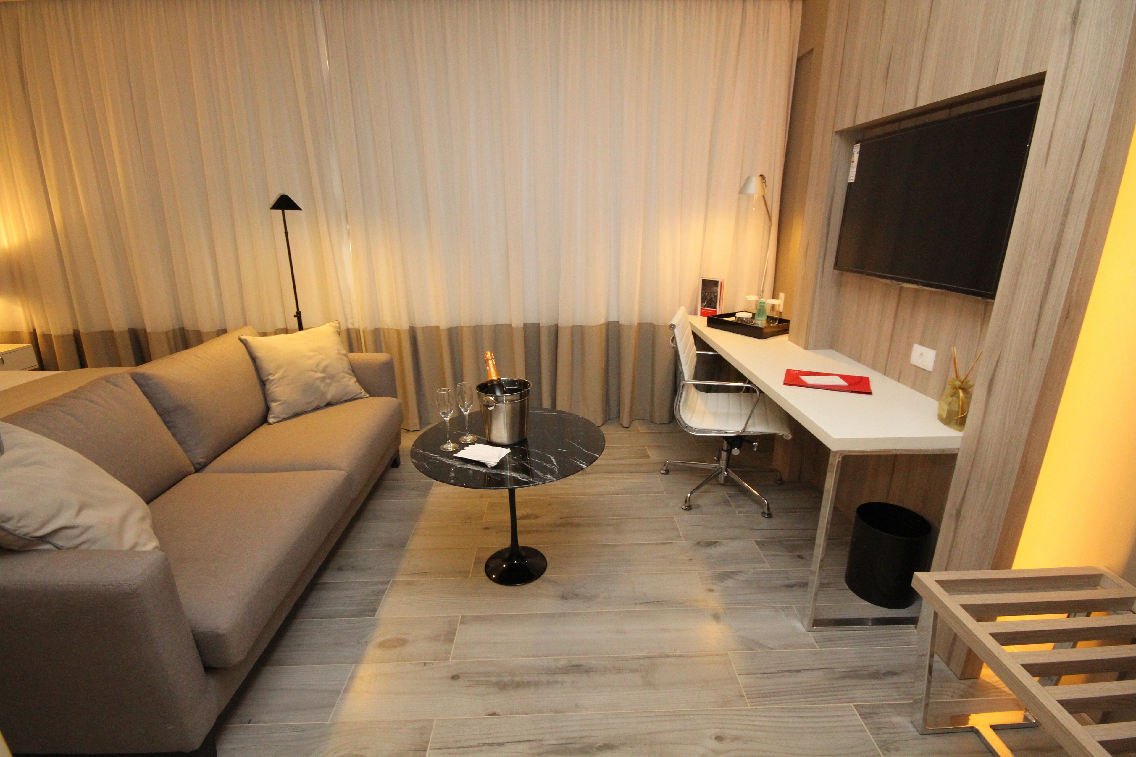 A modern living room with a sofa, a coffee table, a desk, and a TV mounted on the wall.