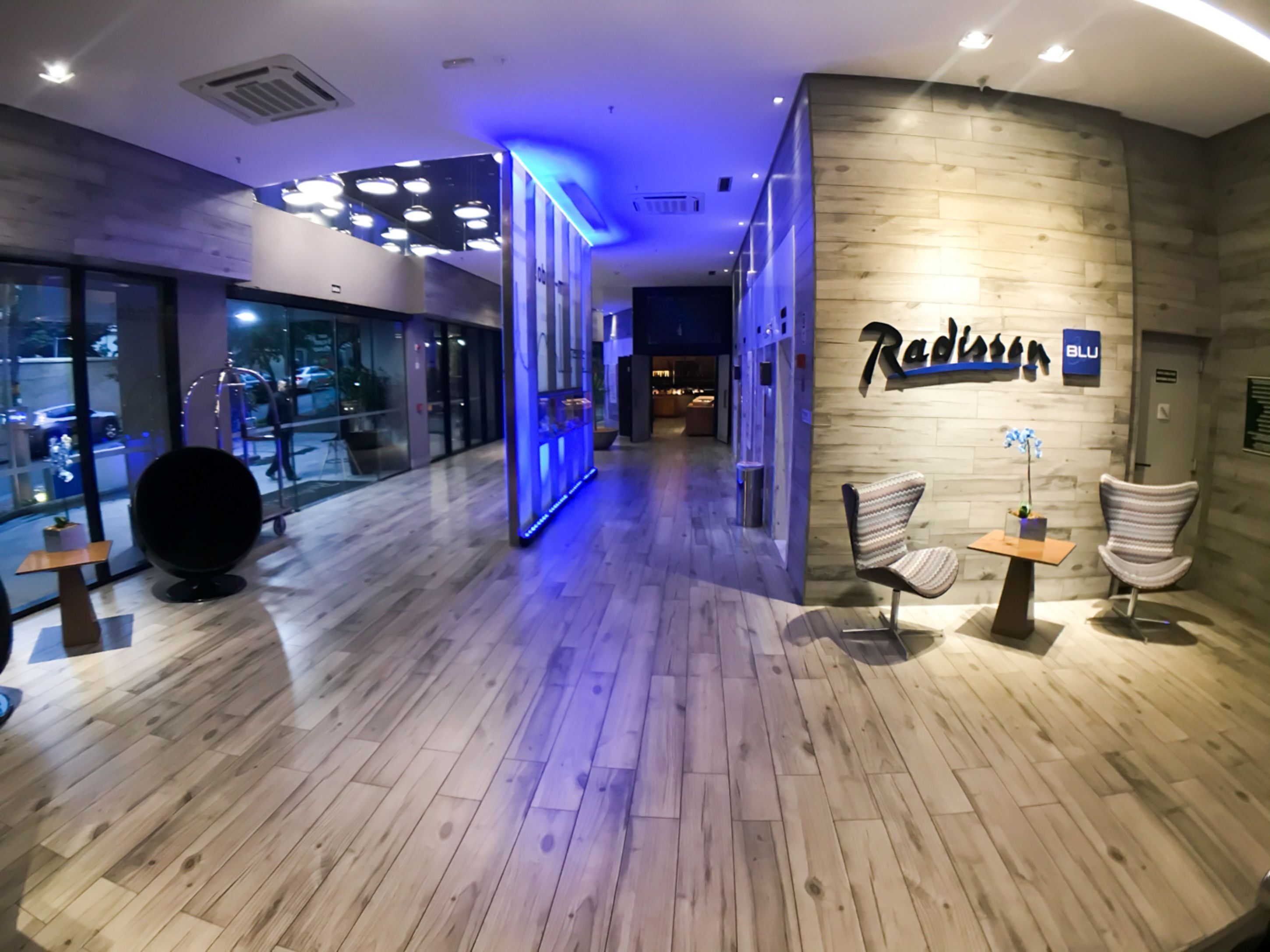A modern hotel lobby with wooden flooring, a reception desk, and a seating area with chairs.