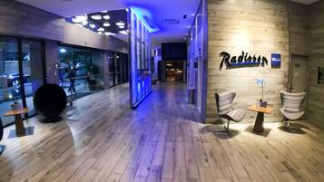 A modern hotel lobby with wooden flooring, a reception desk, and a seating area with chairs.