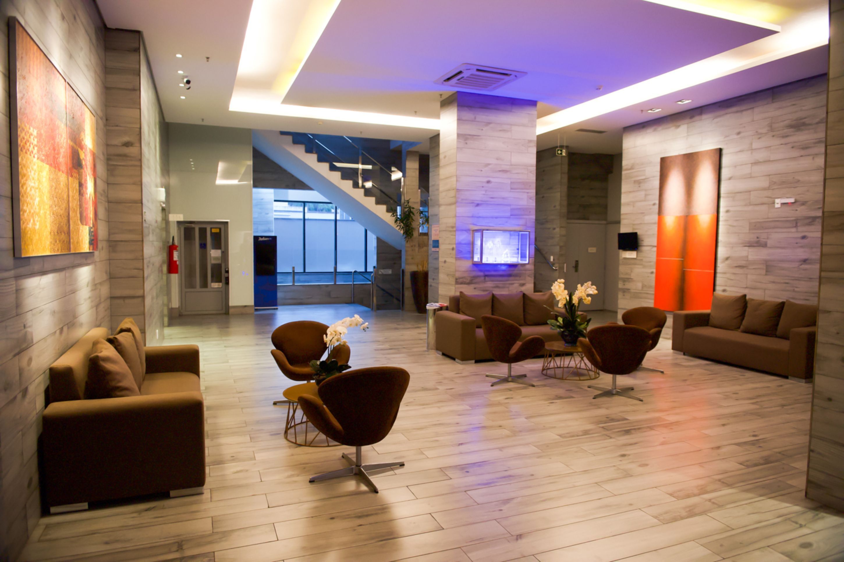 A modern lobby with a wooden floor, brown sofas, and a staircase leading to upper levels.