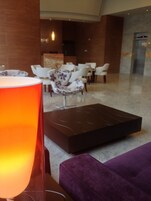 Un vestíbulo moderno con área de descanso, una lámpara naranja grande y un sofá morado.