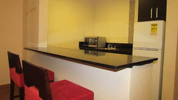 A compact kitchen with a black countertop, a microwave, a refrigerator, and two red chairs.