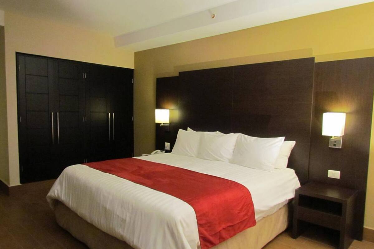 A hotel room with a large bed, two bedside tables, a wardrobe, and wall-mounted lights.