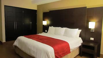 A hotel room with a large bed, dark wooden wardrobe, and bedside lamps.