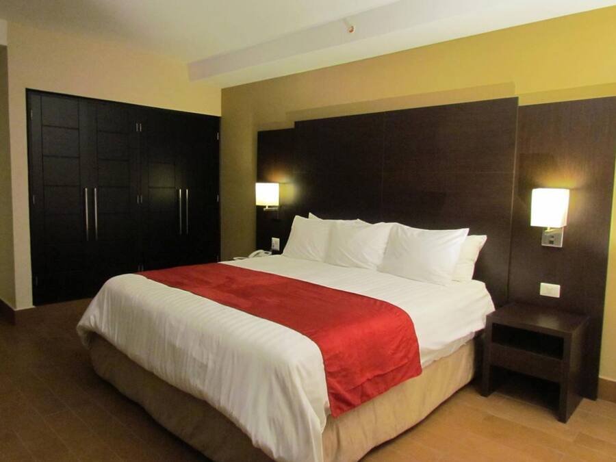 A hotel room with a large bed, dark wooden wardrobe, and bedside lamps.