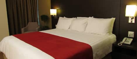 A hotel room with a large bed, a red throw blanket, two bedside lamps, and a telephone on the nightstand.