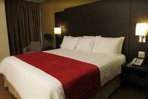 Ein Hotelzimmer mit einem großen Bett, einer roten Tagesdecke, zwei Nachttischlampen und einem Telefon auf dem Nachttisch.