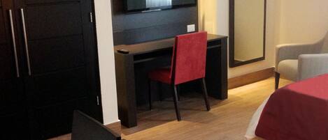 A hotel room with a bed, a desk with a chair, a TV, a wardrobe, and a mirror.