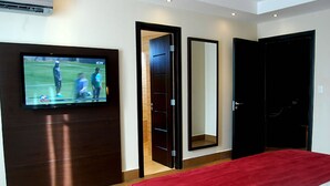 A hotel room with a TV mounted on the wall, a large mirror, and a red bedspread. - Principe Hotel and Suites (Panama City)
