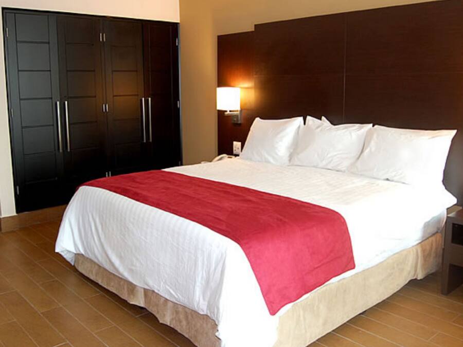Una habitación de hotel con una cama grande, un armario, una mesita de noche y un tocador.