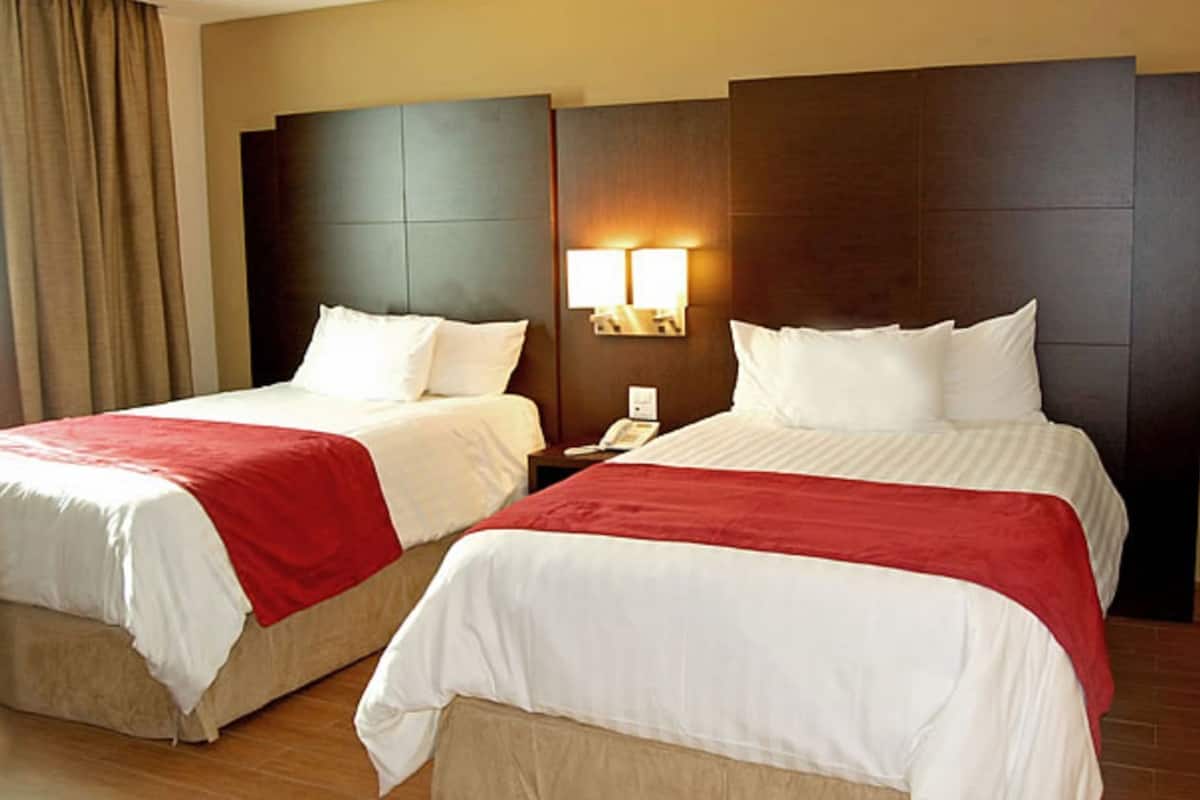 Two double beds with red and white bedding, a nightstand with a phone, and a wall-mounted light fixture.