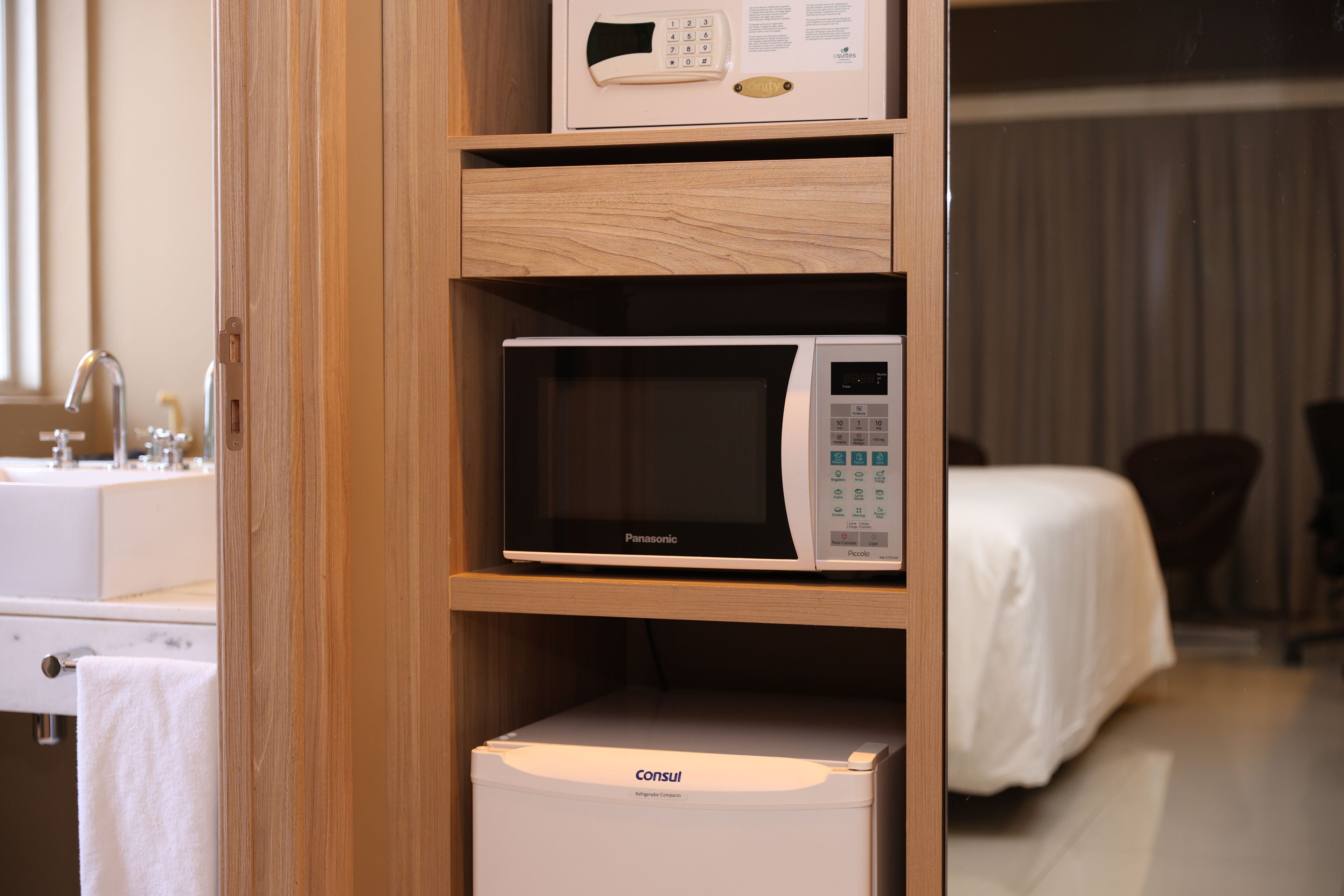 Una habitación de hotel con un mueble de madera que contiene un microondas y una caja blanca con la etiqueta 'Consul'.