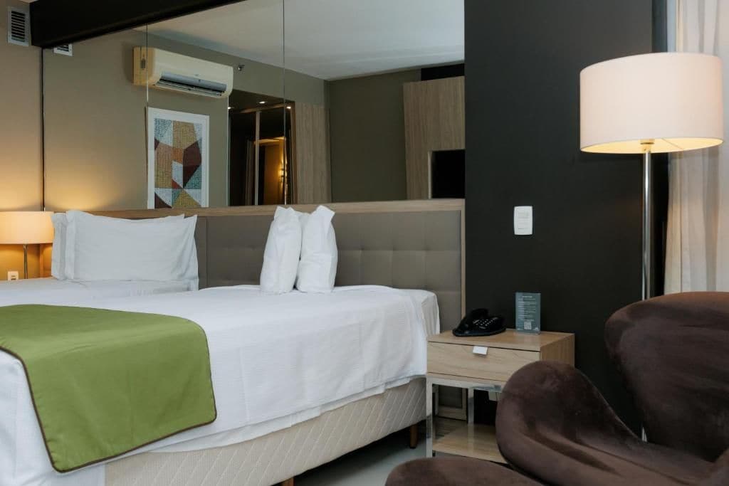 A hotel room with a bed, bedside table, lamp, and a chair.