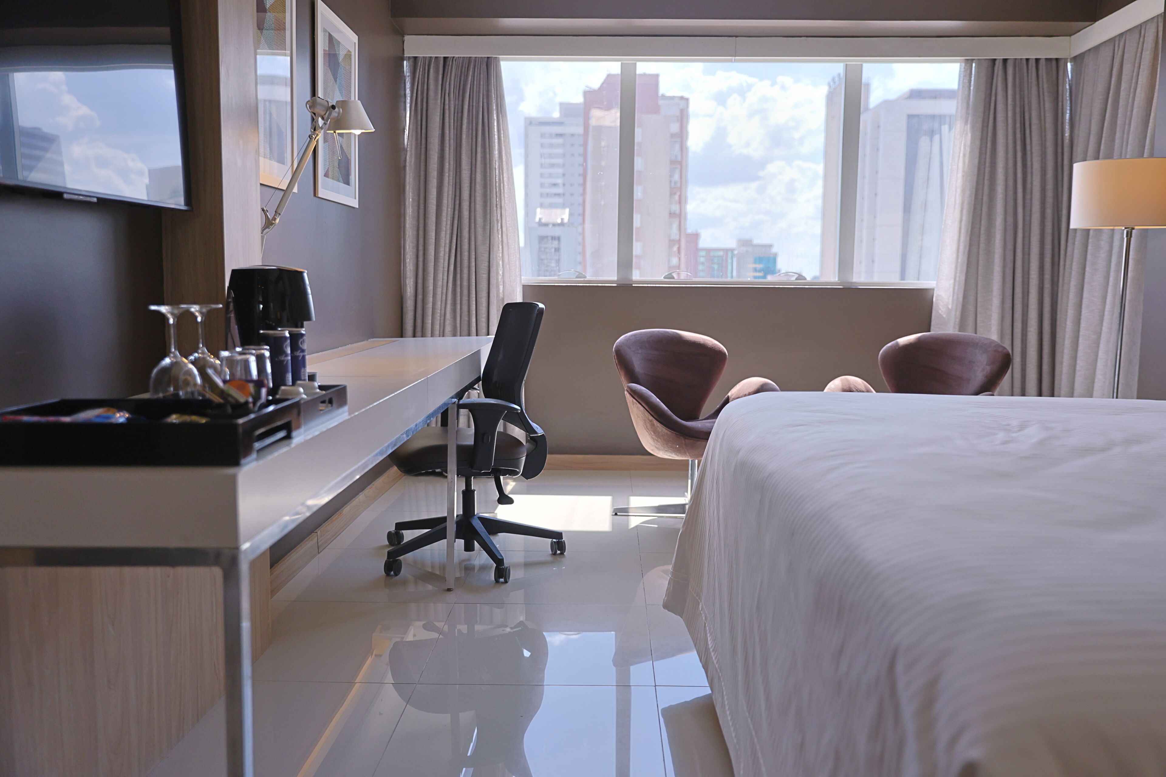 Habitación de hotel con cama, escritorio, silla, televisor y vistas a edificios.