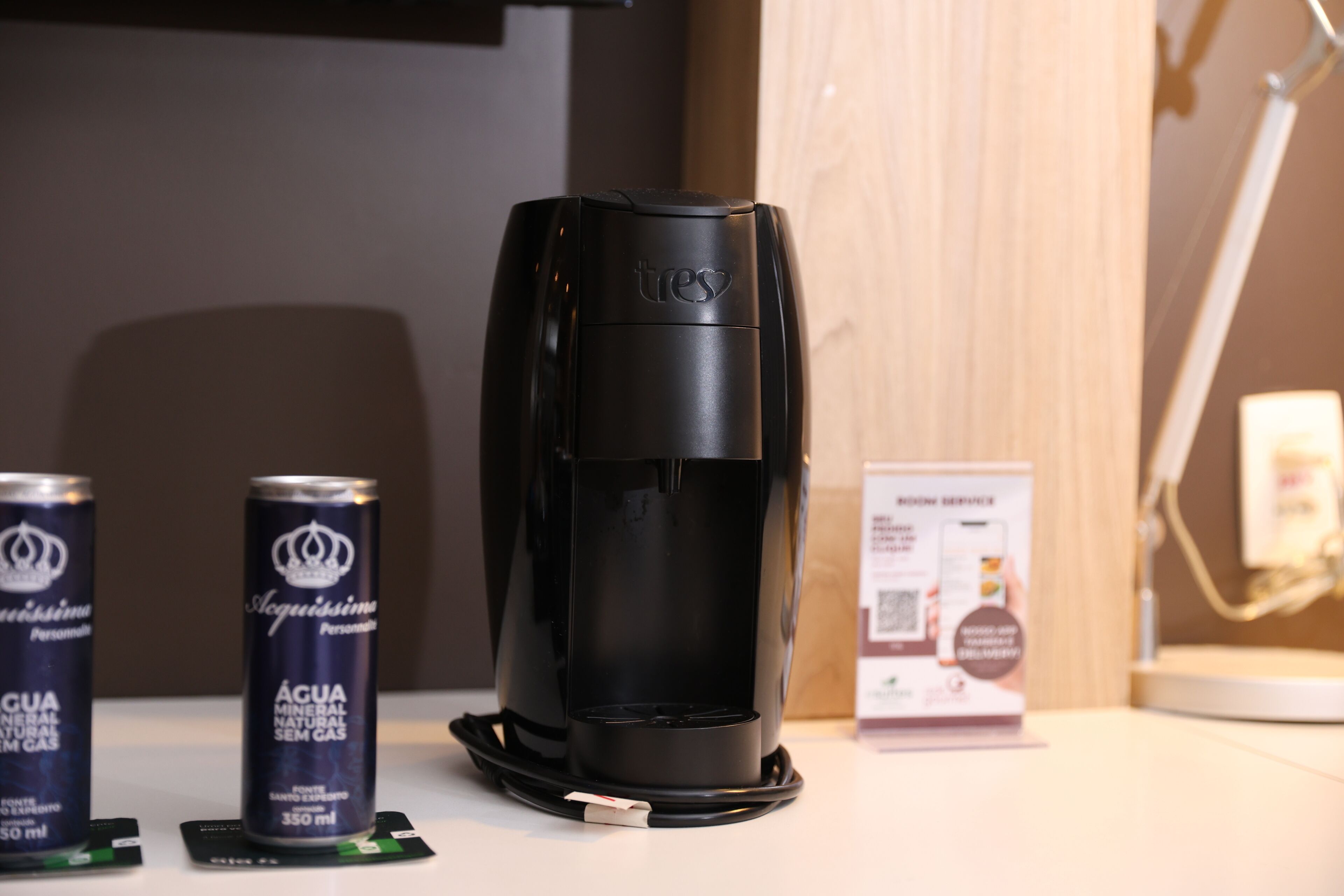 A black coffee maker with a brand name, two cans of water, and a service sign on a counter.
