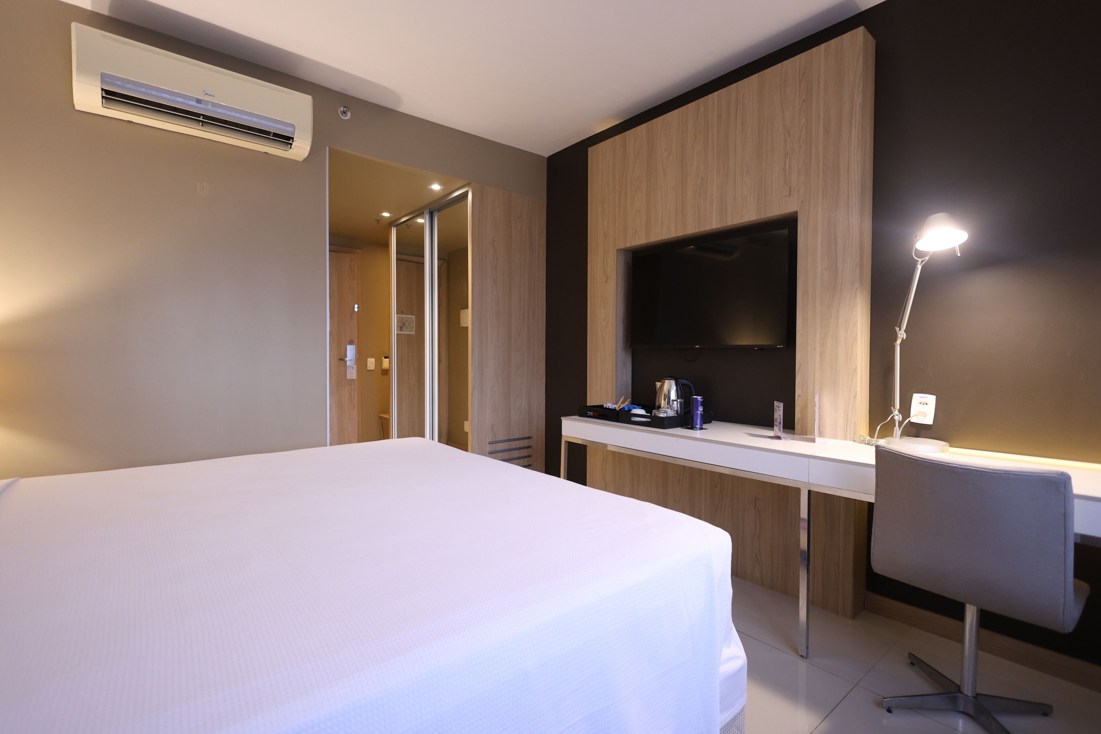 Habitación de hotel con cama, escritorio con televisor de pantalla plana, lámpara de escritorio y aire acondicionado.
