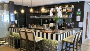 A bar area with a central island, bar stools, and shelves stocked with bottles and glasses.